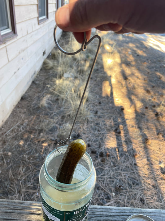 Person using a hook to get a pickle out of a jar outside